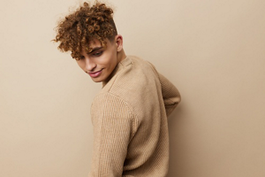 Young man with corkscrew curls wearing a beige jumper